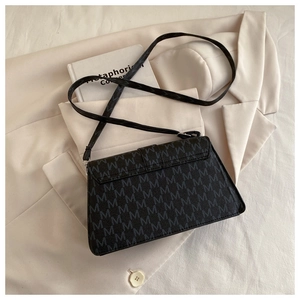 Flat lay of black leather shoulder bag with grey M-letter print on a beige suit