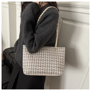 Detail of tweed tote bag showing woven texture and metal chain shoulder strap design