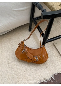 Close-up of brown semi-moon shoulder bag with metal eyelets and star pendant charm