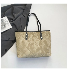 Detail of beige quilted tote bag with black leather handles and golden rivet accents