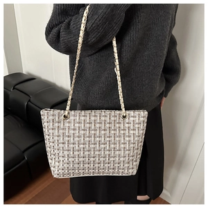 Close-up of checkered tweed tote bag with gold chain strap on a person's shoulder