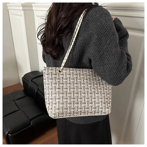 Detail of tweed checkered tote bag featuring a metallic chain strap on a model
