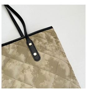 Detail of diamond quilted fabric with black leather handle and golden metal rivets