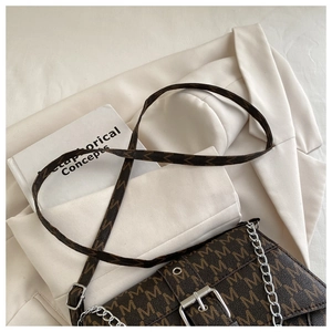 Detailed close-up of brown M-pattern crossbody bag with silver buckle on a blazer