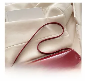 Detail of red patent leather shoulder bag with gold metal buckle and sleek strap