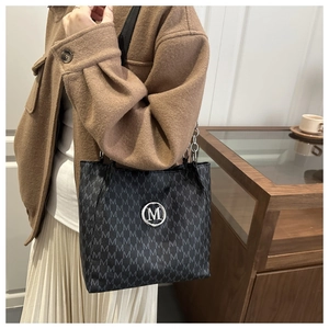 Close-up of black tote bag with letter print pattern and silver round metal M logo