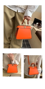 Detail view of bright orange leather handbag with gold twist lock and accordion side pleats
