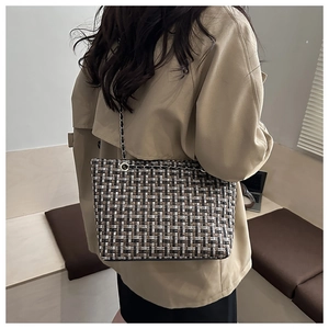 Model wearing a woven plaid tote bag with chain strap for a stylish commuter look