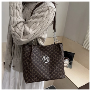Close-up of brown letter print tote bag with silver M logo and metal chain strap