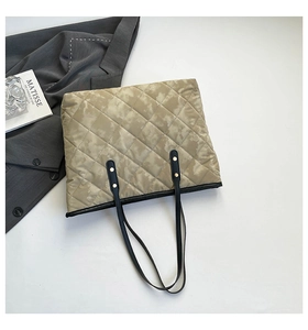 Detailed view of grey quilted tote bag with black handles and artistic book prop