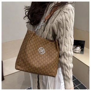 Detail of a brown tote bag with M-pattern print and round silver metallic logo emblem