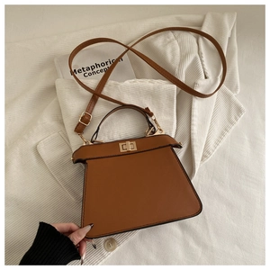 Close-up of brown synthetic leather handbag with gold metal twist lock and trapezoid design