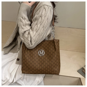 Détail d'un sac cabas marron avec imprimé monogramme M et logo en métal argenté