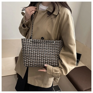 Classic tweed tote bag with metal chain strap worn over a khaki trench coat