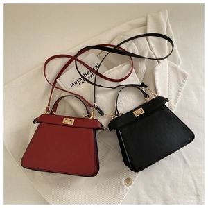 Detail of burgundy and black trapezoid handbags with gold turn-lock and shoulder straps