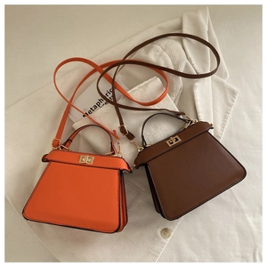 Detail view of leather trapezoid handbags with twist lock and strap in orange and coffee