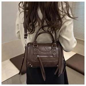 Detail view of dark brown biker bag with silver studs and long fringe tassels