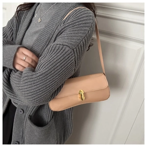 Close-up of a cream-colored baguette bag with a gold twist lock on a gray cardigan