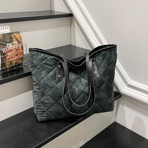 Black quilted tote bag with large capacity and gold rivets on a stylish staircase