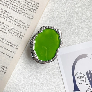Close-up of a silver textured metal phone grip with glossy green resin center on a book