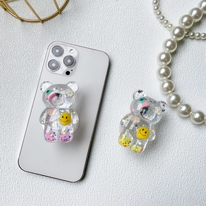 Cute bear-shaped resin phone socket with glitter and smiley face on a white smartphone
