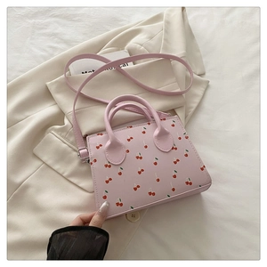 Détail d'un sac à bandoulière rose avec imprimés cerises sur un blazer beige chic