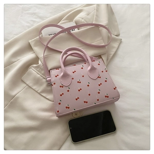 Détail du sac bandoulière rose en similicuir à imprimé cerise sur fond de costume crème