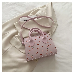 Détail du mini sac à main rose à motif cerise sur un blazer beige en lumière naturelle