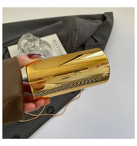 Close-up of a gold metal hard shell clutch bag with a slim chain and polished finish