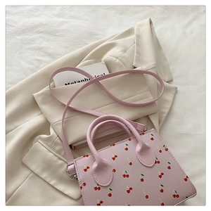 Détail du sac à main rose à imprimé cerise posé sur un blazer beige avec un livre