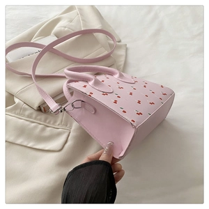 Détail du sac à main rose à motif cerise sur un blazer blanc avec boucles argentées