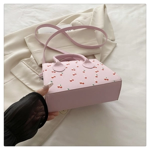 Detailed shot of pink cherry print handbag with top handle and crossbody strap
