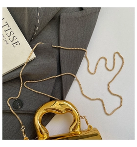 Detail of mirror gold handbag featuring an irregular wave handle and metal chain strap