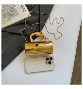Detail of gold metal cylinder handbag with unique handle next to a phone for scale