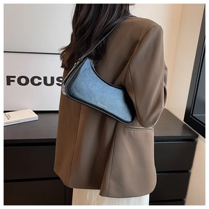 Fashionable black half-moon shoulder bag shown on shoulder of a woman in a suit