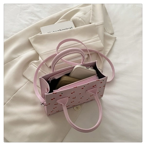 Détail du sac à main rose avec imprimé cerise, cuir souple et bandoulière amovible