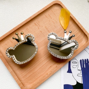 Close-up of rhinestone bear-shaped makeup mirror with crown detail in a wooden tray