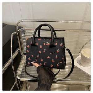 Close-up detail of black PU leather tote bag with red cherry print and round handles