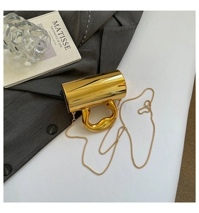Detail view of mirror gold crossbody bag with unique handle and chain on grey suit