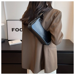 Side view of a chic black leather underarm bag worn by a model in a minimalist room