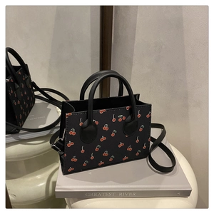 Detail of black cherry print handbag with cylindrical handles and crossbody strap