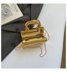 Detail of a luxury gold metallic box clutch bag with elegant curved handle and ball chain
