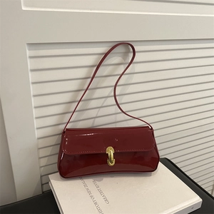 Schicke dunkelrote Lackleder-Achseltasche mit goldener Hufeisenschnalle auf Buch