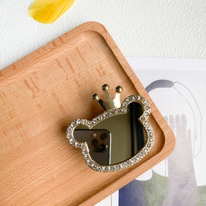 Macro detail of rhinestone crown bear phone grip and makeup mirror on wooden tray