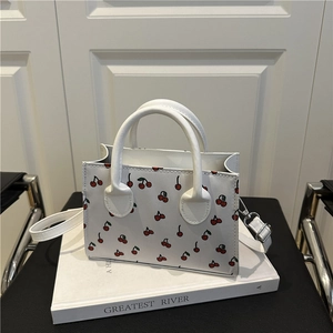 White cherry print tote bag with dual handles and detachable shoulder strap on white book