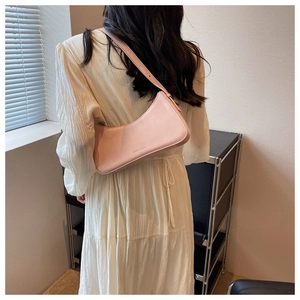 Detailed view of a light pink Hobo underarm bag worn on a white dress in a minimalist room