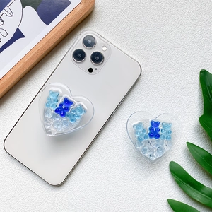Cute heart-shaped cell phone grip with blue gummy bear charms for steady desktop viewing