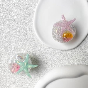 Detail of glitter starfish and seashell resin phone grips on a white ceramic plate