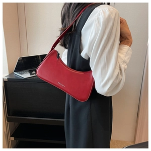 Detail of red faux leather baguette bag showing silver logo and smooth texture on a model