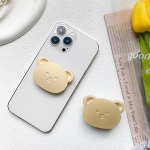 Detail of cute gold bear phone socket holder mounted on a white smartphone on a desk